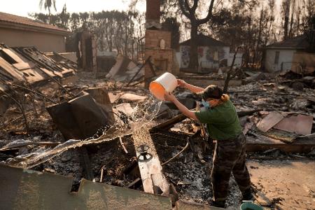 Nancy Belanger gießt Wasser auf das vom Feuer verwüstete Grundstück eines Nachbarn im Stadtteil Pacific Palisades von Los Angeles.