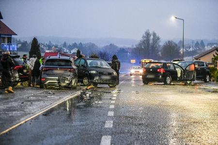 Nach einem Unfall bei Glatteis mit mehreren Fahrzeugen in Baden-Württemberg stehen Helfer und Beteiligte an den Autos auf einer Straße. 