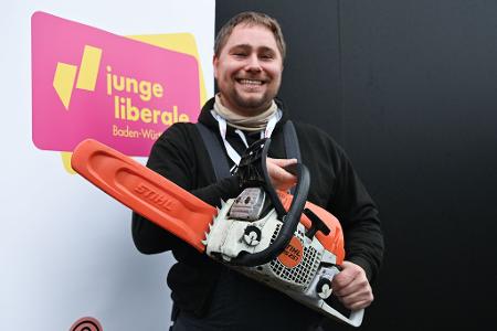 Mit der Kettensäge will Mark Hohensee, Landesvorsitzender der Jungen Liberalen, packt für den Bürokratieabbau symbolisch die Kettensäge aus. 