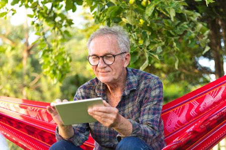 Mann mit Tablet sitzt in einer Hängematte