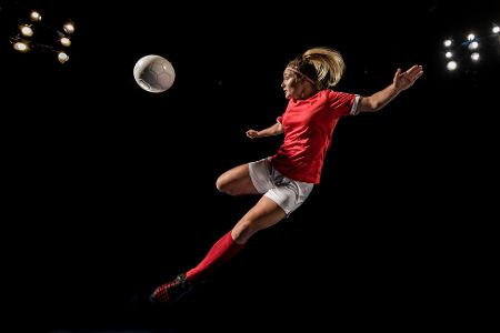 Fußballerin im Sprung tritt nach dem Ball vor schwarzem Hintergrund