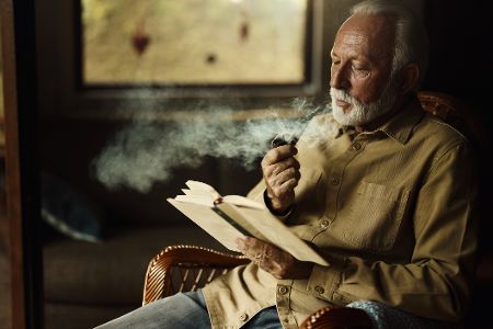 Älterer Mann raucht beim Lesen eines Buches Pfeife