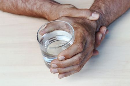 Hand eines älteren Menschen hält ein Glas Wasser, die andere stützt sie dabei