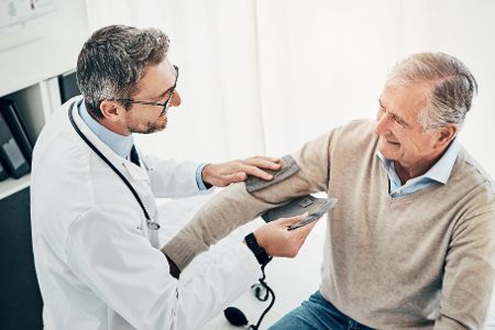 Arzt misst bei älterem Patienten Blutdruck