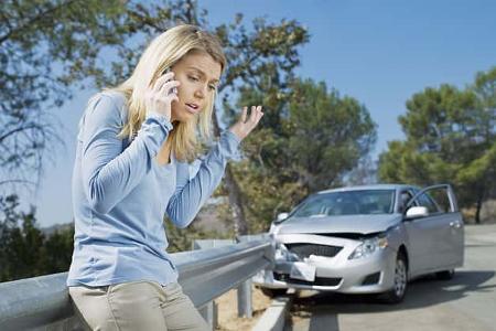 Frustrated woman using cell phone next to car wrecked on guardrail