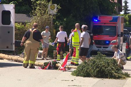 Der umgestürzte Maibaum liegt auf der Straße vor einem Einsatzwagen der Feuerwehr. Der umgestürzte Maibaum liegt auf der Straße vor einem Einsatzwagen der Feuerwehr.