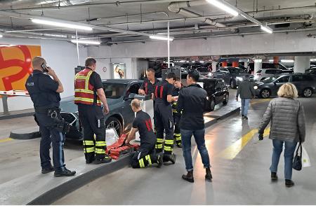 Einsatzkräfte der Feuerwehr mit der demontierten Schranke, wartende Fahrzeuge fahren aus dem Parkhaus Einsatzkräfte der Feuerwehr mit der demontierten Schranke, wartende Fahrzeuge fahren aus dem Parkhaus