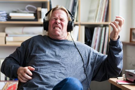 Älterer Mann hört mit geschlossenen Augen Musik und imitiert Gitarrenspiel