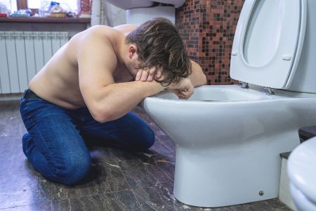 Mann kniet neben einer Toilette und hat einen Kater