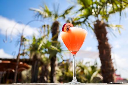 Ein Passionsfrucht Martini (auch Pornstar Martini oder Maverick Martini genannt) steht unter Palmen auf einem Tisch in einer Strandbar. Ein Passionsfrucht Martini (auch Pornstar Martini oder Maverick Martini genannt) steht unter Palmen auf einem Tisch in einer Strandbar.