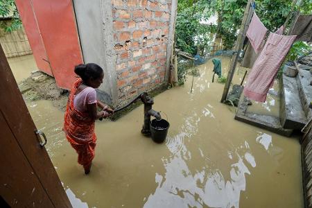 Eine Frau versucht in der überfluteten Umgebung ihres Hauses, Wasser zu sammeln. Eine Frau versucht in der überfluteten Umgebung ihres Hauses, Wasser zu sammeln.