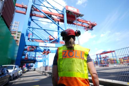 Eine Zollbeamtin steht neben einem Containerschiff im Hamburger Hafen. 