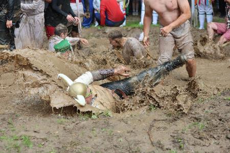 Teilnehmer springen auf dem Dreckschweinfest 2025 auf dem Festivalgelände auf der Wildbahn in ein Schlammloch. 