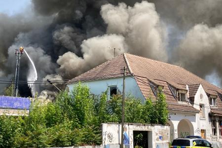 Auf dem alten Schlachthofgelände in Erfurt ist ein Feuer ausgebrochen und Rauch steigt in den Himmel, während die Feuerwehr gegen die Flammen kämpft.