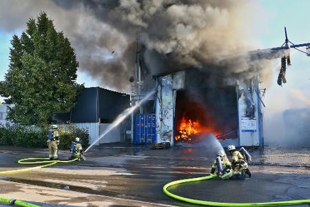 Feuerwehrleute löschen den Brand einer Halle und mehrerer Silos auf einem Firmengelände. Weil die Polizei eine politisch motivierte Brandstiftung im Kontext des Krieges zwischen Israel und dem Iran nicht ausschließt, ermittelt auch der Staatsschutz.