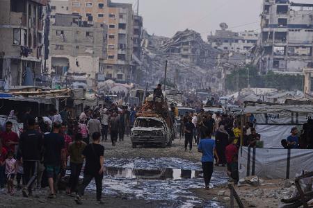 Möbel und eine Matratze werden mit einem beschädigen Auto zwischen Fußgängern durch einen Markt in Gaza-Stadt transportiert.