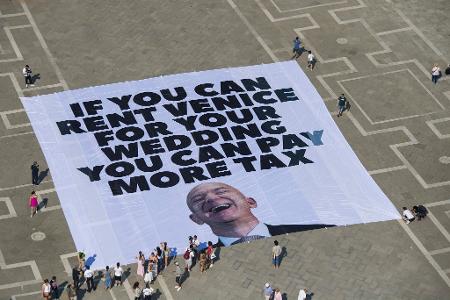 Mit einem Plakat auf dem Markusplatz fordern Greenpeace-Aktivisten, Bezos höher zu besteuern.