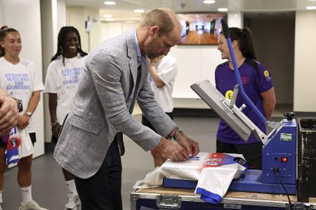 Prinz William (M) druckt eine Rückennummer auf ein Trikot der englischen Frauennationalmannschaft.