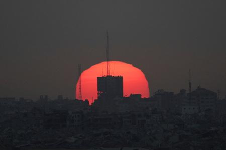 Die Sonne geht hinter beschädigten Gebäuden im Gazastreifen unter, vom Süden Israels aus gesehen.