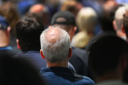 In einer Menschenmenge ist ein Mann mit weißen Haaren und teilweiser Glatze von hinten zu sehen