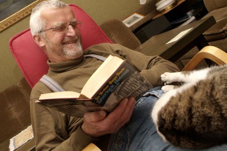 Älterer Mann sitzt in einem Sessel, hat ein Buch in der Hund und seine Katze auf dem Schoß