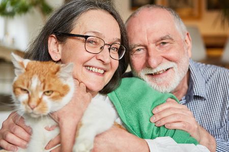 Älteres Paar mit Katze auf dem Arm schaut glücklich