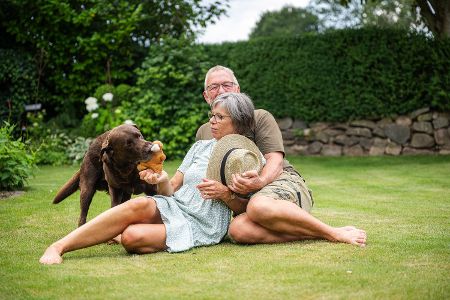 Rentnerpaar sitzt mit Hund auf dem Rasen im Garten Rentnerpaar sitzt mit Hund auf dem Rasen im Garten
