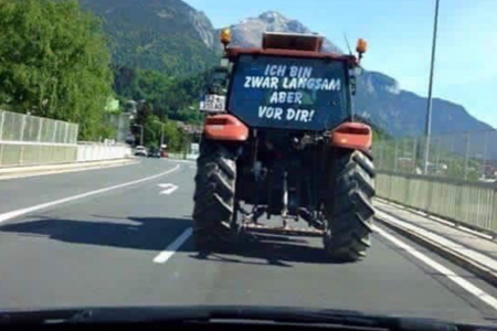 Trecker auf einer Straße vor einem Auto mit Schild hinten dran