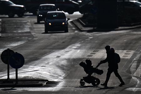 Mutter mit Kinderwagen geht über eine Straße zu einer Verkehrsinsel