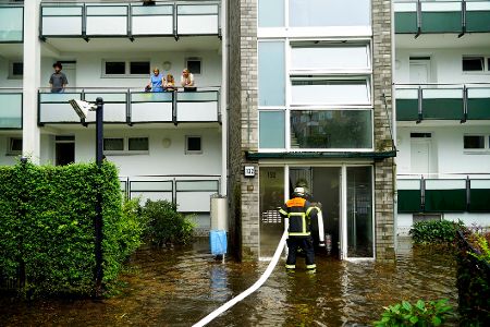 Feuerwehrmann steht im Eingang eines mit Wasser vollgelaufenen Mehrfamilienhauses und pumpt Wasser ab