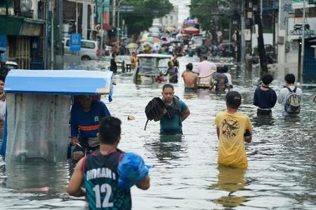 Anwohner waten durch eine überschwemmte Straße auf den Philippinen.