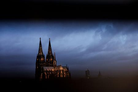 Der Dom in Köln ist am Morgen durch ein Geländer gesehen beleuchtet.