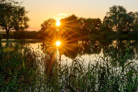 Die untergehende Sonne spiegelt sich in einem kleinen See im östlichen Brandenburg.