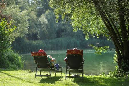 Sommerwetter in Deutschland. Ein Mann und eine Frau liegen am Ufer des Schwarzachtalsees in Liegestühlen und sonnen sich.