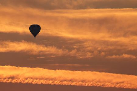Ein Ballon ist am Morgen kurz vor Sonnenaufgang am orange gefärbten Morgenhimmel zu sehen.