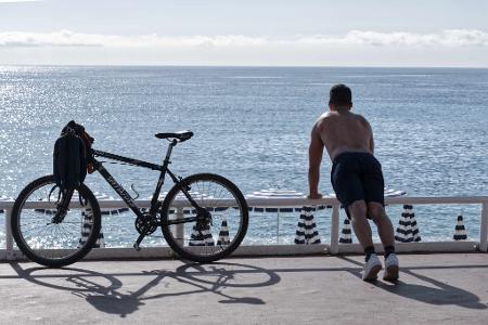 Ein Mann mit nacktem Oberkörper macht am Strand von Nizza neben seinem Fahrrad Übungen. (Archivbild)