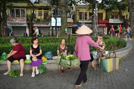 Eine Verkäuferin verkauft Gemüse an Menschen in Hanoi, die in einem Park Morgensport treiben.