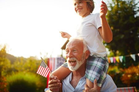 Älterer Mann hat kleines Kind auf den Schultern und eine US-Flagge in der Hand