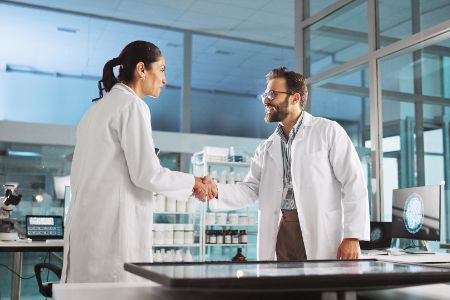 Zwei Wissenschaftler reichen sich in einem Labor die Hand
