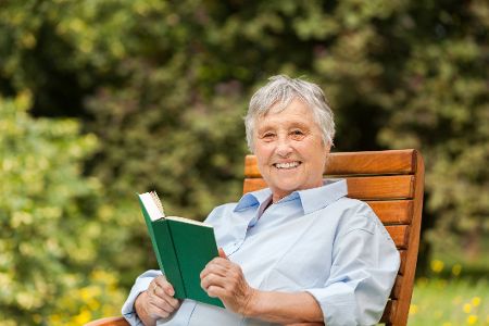 Alte Frau mit Buch in der Hand sitzt lächelnd draußen