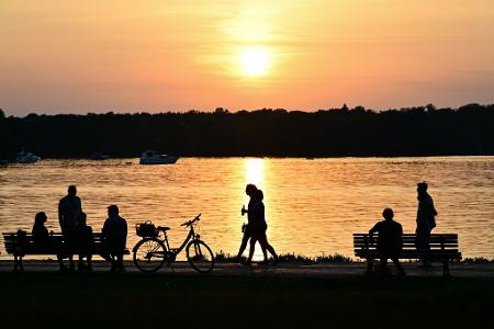 Menschen gehen bei Sonnenuntergang am Ufer des Tegeler Sees in Berlin.