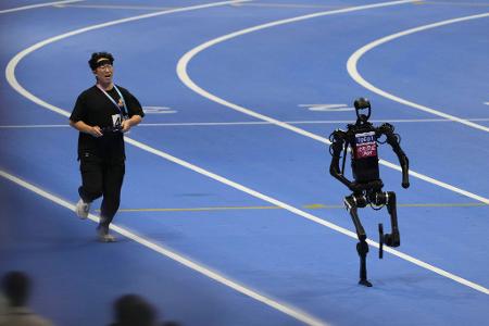 Ein menschlicher Bediener versucht, mit einem Roboter im 1500-Meter-Lauf bei den World Humanoid Robot Games in Peking Schritt zu halten.