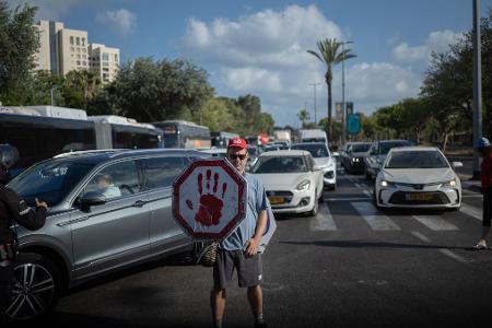 Ein israelischer Demonstrant geht mit einem Schild auf einer Straße, während Autos sich stauen. 