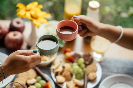 Zwei Menschen stoßen mit Kaffeetassen über einem gedeckten Tisch an