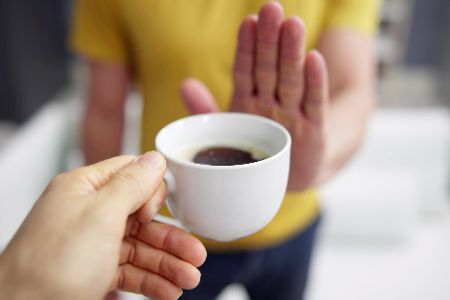 Mensch lehnt Tasse Kaffee mit der Hand ab