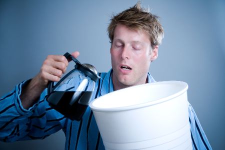 Übernächtigter Mann mit voller Kaffeekanne in der Hand gießt sich Kaffee in eine gigantische Tasse