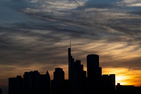 Die Hochhäuser der Bankenskyline von Frankfurt zeichnen sich silhouettenhaft vor der untergehenden Sonne ab.