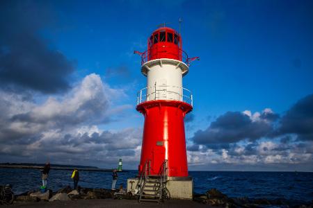 Angler stehen neben dem Leuchtfeuer auf der Ostmole an der Hafeneinfahrt in Warnemünde.