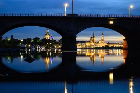 Blick am Abend in Dresden durch die Brückenbögen der Albertbrücke auf die historische Altstadtkulisse an der Elbe mit der Frauenkirche (l-r), der Kuppel der Kunstakedmie mit dem Engel „Fama“, dem Terrassenufer, dem Ständehaus, dem Hausmannsturm, der Hofkirche und der Semperoper.