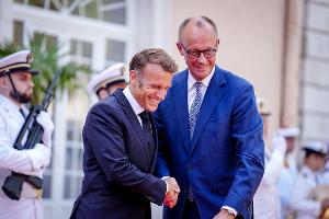 Wie zwei alte Freunde begrüßen sich Macron und Merz vor dem Fort du Cap Brun über der Cote d'Azur.